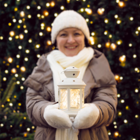 An adult woman in winter clothes holds a glowing flashlight and smiles against the background of a Christmas tree with a garland of lights.の写真素材