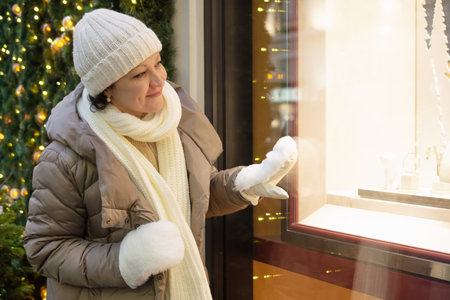 An adult woman in winter clothes looks at a Christmas shop window and smiles.の写真素材