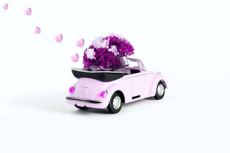 Russia. Moscow. 07.02.2021 Pink car with a bouquet of flowers on a white background from which hearts are flying. Holiday concept, transportation.の写真素材