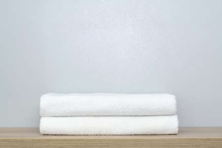 A view of two neatly folded white bath towels on a wooden shelfの写真素材