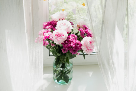 View of a bouquet of pink peonies and chrysanthemums in a vase on the window. Concept background, flowers, holidayの写真素材