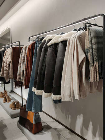 Rack with clothes on hangers and shoes in the store against the background of a small wallの写真素材