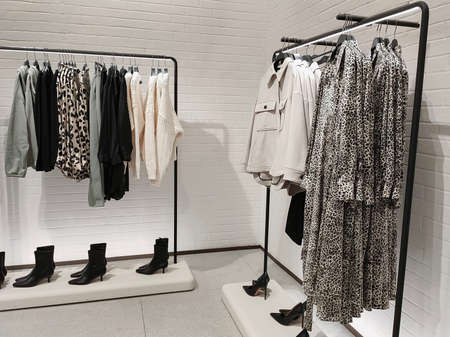 Rack with clothes on hangers and shoes in the store against a small wall.の写真素材