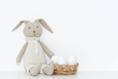 Easter composition with a soft rabbit toy and white eggs in a basket on a shelf in the roomの写真素材