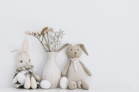Easter composition with soft toys of hares and white eggs that are on the shelf in the roomの写真素材