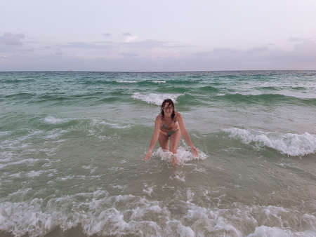 A young woman in a swimsuit runs into the sea on the waves and laughs.の写真素材