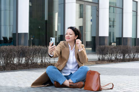 An adult woman sits on the sidewalk and speaks via video link with a joyful expression on her face.の写真素材