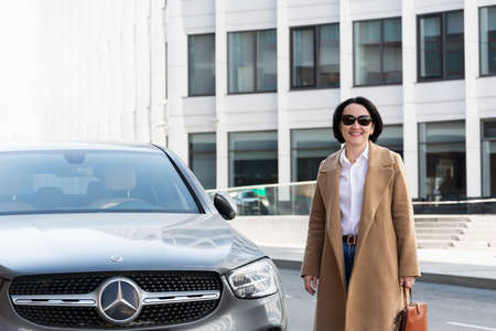 11.04.2021 Russia. Moscow A beautiful confident woman stands near a Mercedes car and smiles.のeditorial素材