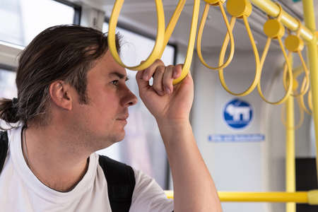 A young man rides in public land urban transport holding on to the yellow handrails.の写真素材