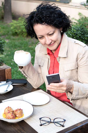 woman with a mobile phone in her hands communicates online while sitting in a cafeの写真素材