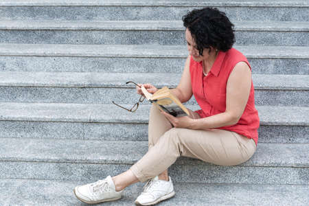 A woman sits on the steps in the city and reads a book.の写真素材