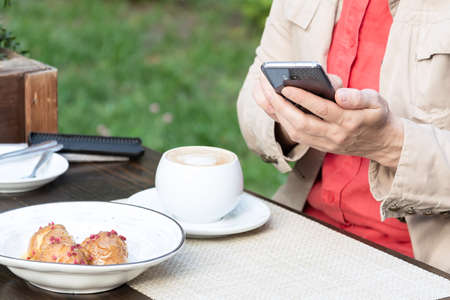 A woman sits in a cafe on the street over a cup of coffee and sends messages on the phone.の写真素材