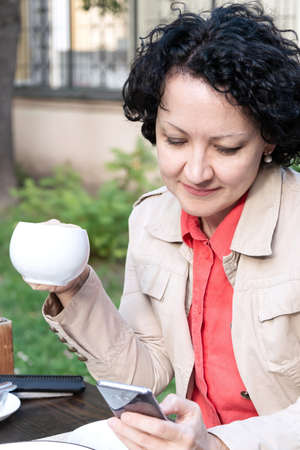 woman with a mobile phone communicates online while sitting in a cafe over a cup of coffeeの写真素材