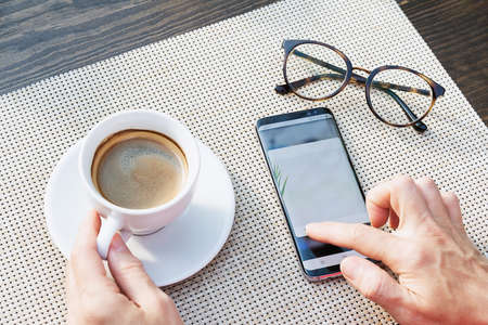top view of a cup of coffee glasses and hands who are typing a message on the phoneの写真素材