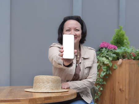 Happy woman sits at a table in a cafe and shows the white screen of the phone.の写真素材