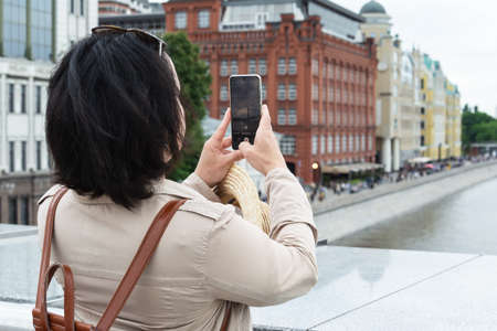 An adult dark-haired woman takes photographs of landmarks on her phone while traveling.の写真素材