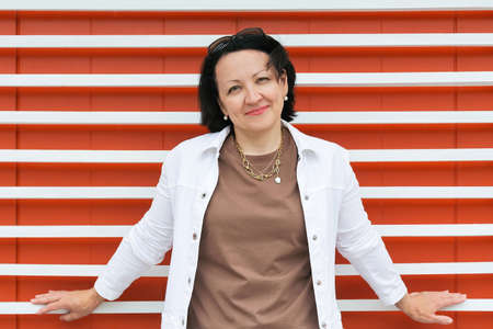 Portrait of a mature smiling woman in summer clothes on a bright orange background with a white stripe.の写真素材