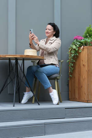 A woman is sitting at a table in a cafe with a phone in her hands and talking via video link.の写真素材