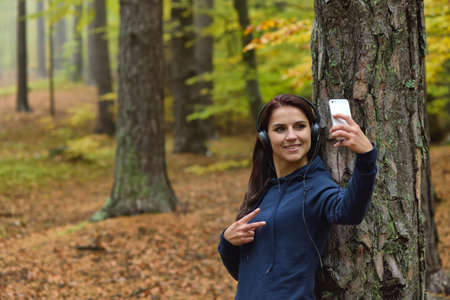 Girl listens to music and making selfie with smartphone in nature. Autumn forrest in the backgroundの写真素材