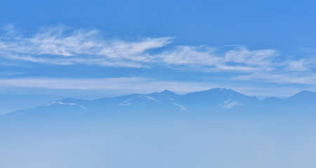 Beautiful view of mountain peak with sunrise light on top against blue sky with clouds in a foggy dayの写真素材