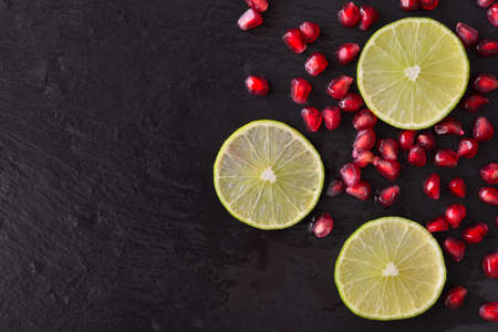 Fresh ripe pomegranate seeds and lime slices on wet black stone vintage backgroundの写真素材