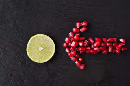 Fresh ripe pomegranate seeds and lime slices on wet black stone vintage backgroundの写真素材