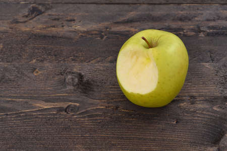 One bitten green apple on a brown wooden desk, top angle viewの写真素材