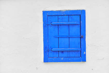 Closed vintage blue window on white wall of old house in romaniaの写真素材