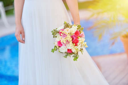 Bride in wedding dress holds her rouses bouquet against blue poolの写真素材