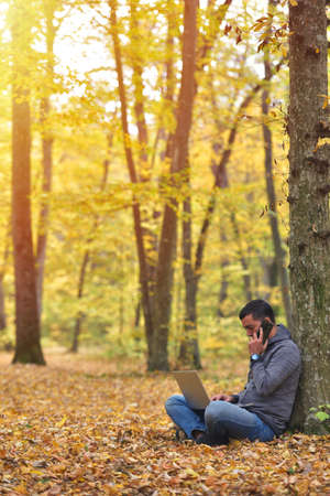 Man with laptop and smartphone in forest, autumn colors, sunset warm lightの写真素材