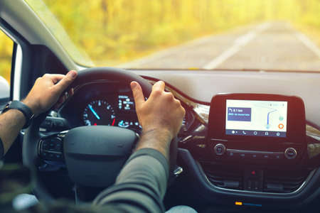 Male driver with hands on the steering wheel driving on road in autumn warm colorsの写真素材