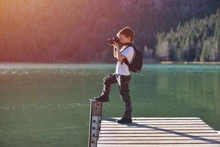 Creative child, kid photographer (a little boy) with a camera taking landscape pictures near la lakeの写真素材