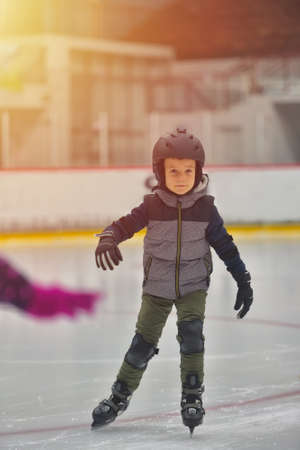 Adorable little boy in winter clothes with protections skating on ice rinkの写真素材