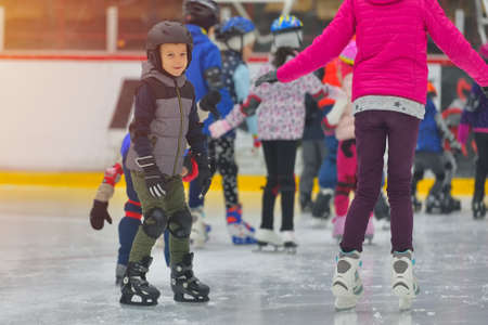 Adorable little boy in winter clothes with protections skating on ice rinkの写真素材