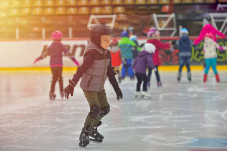 Adorable little boy in winter clothes with protections skating on ice rinkの写真素材