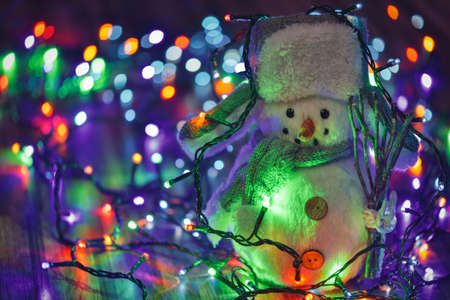 Small toy snowman on colorful Christmas lights backgroundの写真素材