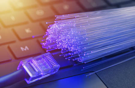 Fiber optics in blue, close up with network and keyboard background, warm lens flare