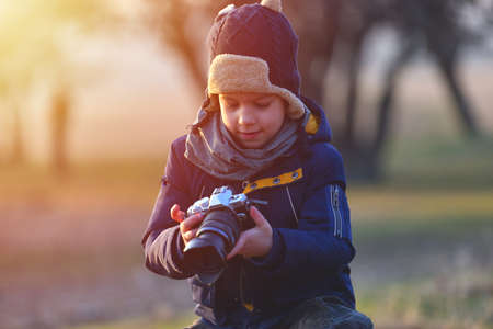 Creative child, kid photographer (a little boy) with a camera taking landscape pictures in warm sunset lightの写真素材