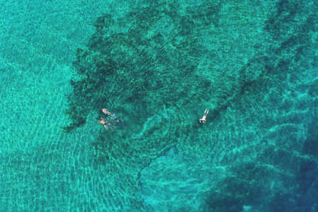Father and son snorkels through tropical, turquoise waters, aerial viewの写真素材