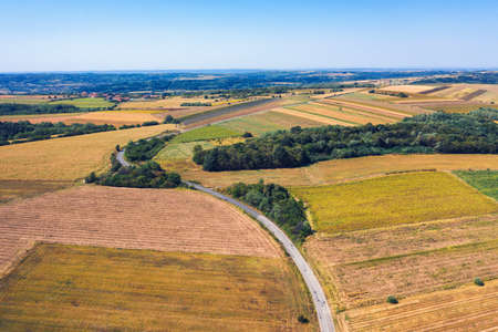 Aerial view of a country road amid fields against blue clear sky
