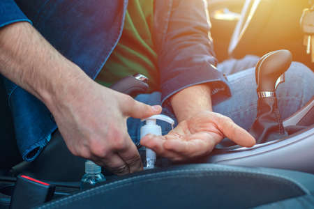 Man sitting in the car disinfect his hands to avoid coronavirus infection. Close-up on hands. Man using hand sanitizer in the car.の写真素材