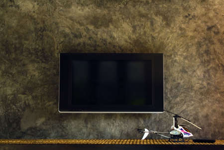 LCD TV mounted in front of cement wall by a toy helicopter