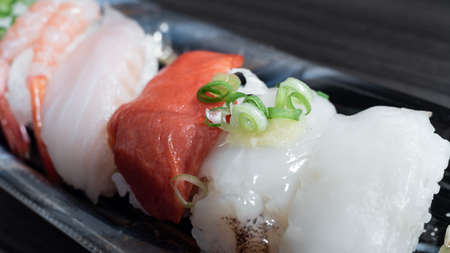 Closeupâ piecesâ ofâ sushiâ withâ a variety ofâ rawâ meat toppingsâ onâ a plasticâ container.の写真素材