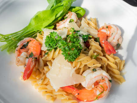 Closeupâ fusilli onâ whiteâ plateâ withâ prawns, parsley sprigs, greenâ leaves, andâ cheese flakes.の写真素材