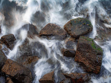 Slow speed shot of rock-bound coast with silky water waving back to the sea.の写真素材
