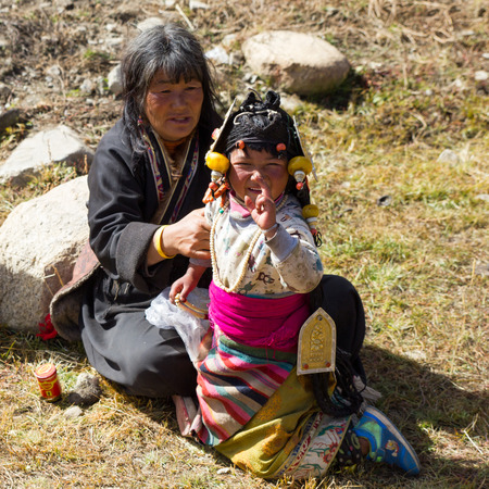 Yading, China - October 27 2016: A young girl in a traditional Tibetan costume manages a slight frown at the camera as another girl in the background looks on.のeditorial素材