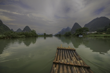 drifting on a wooden raft in a picturesque rural countryside with rolling hills on a cloudy dayの写真素材