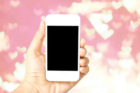 Hand holding smart phone on heart shaped bokeh pink defocused  backgroundの写真素材