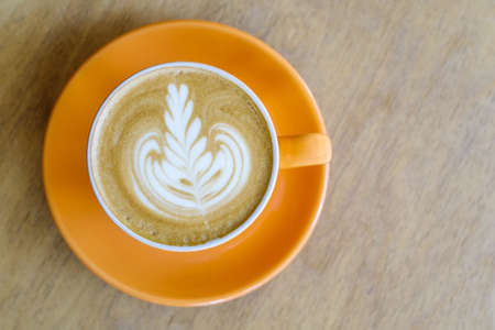 Top viiew of hot coffee latte with foam latte art on orange plate and wood backgroundの写真素材
