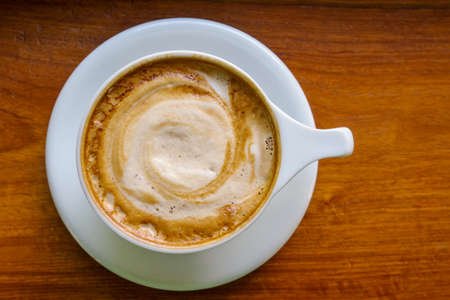 Top view of cappuccino coffee cup with milk foam on wood background